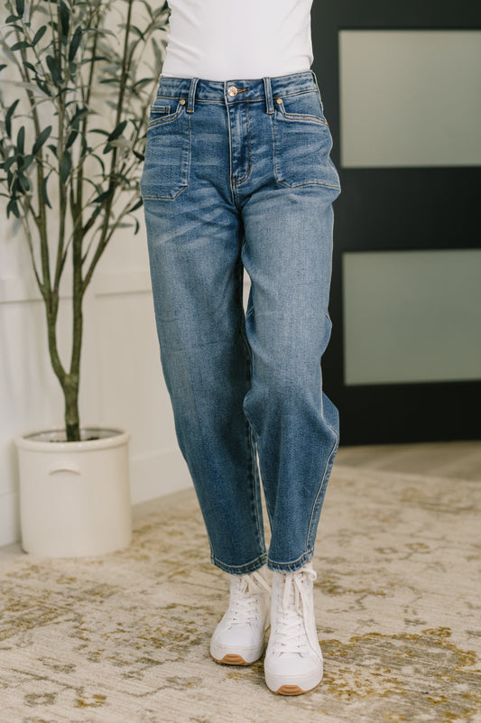 Person wearing blue jeans and white sneakers standing in a room with a plant and striped wall.