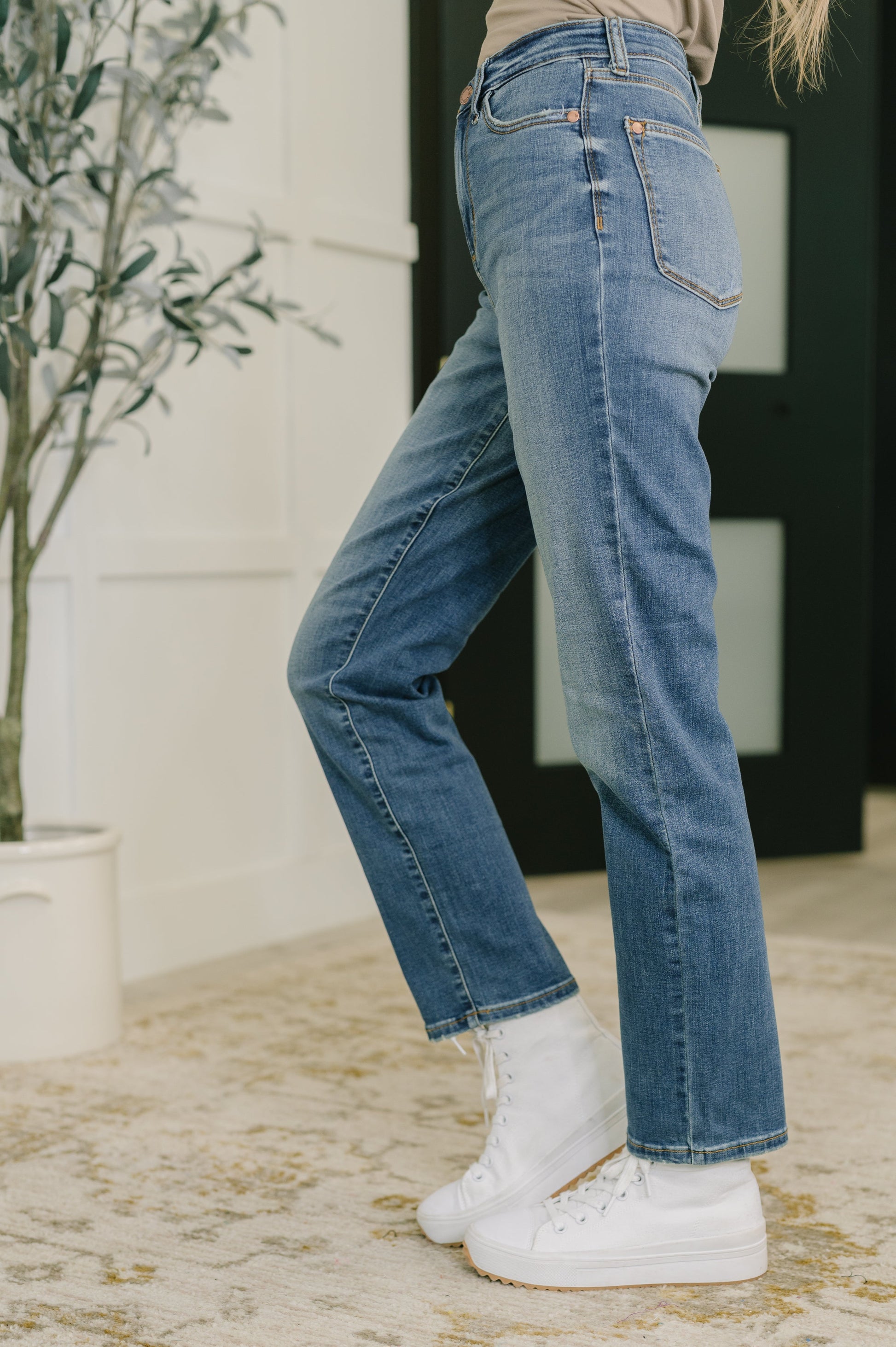 Person wearing blue jeans and white sneakers in a blurred indoor setting