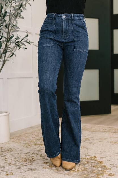Blue jeans worn by a person standing indoors with a plant and wall in the background