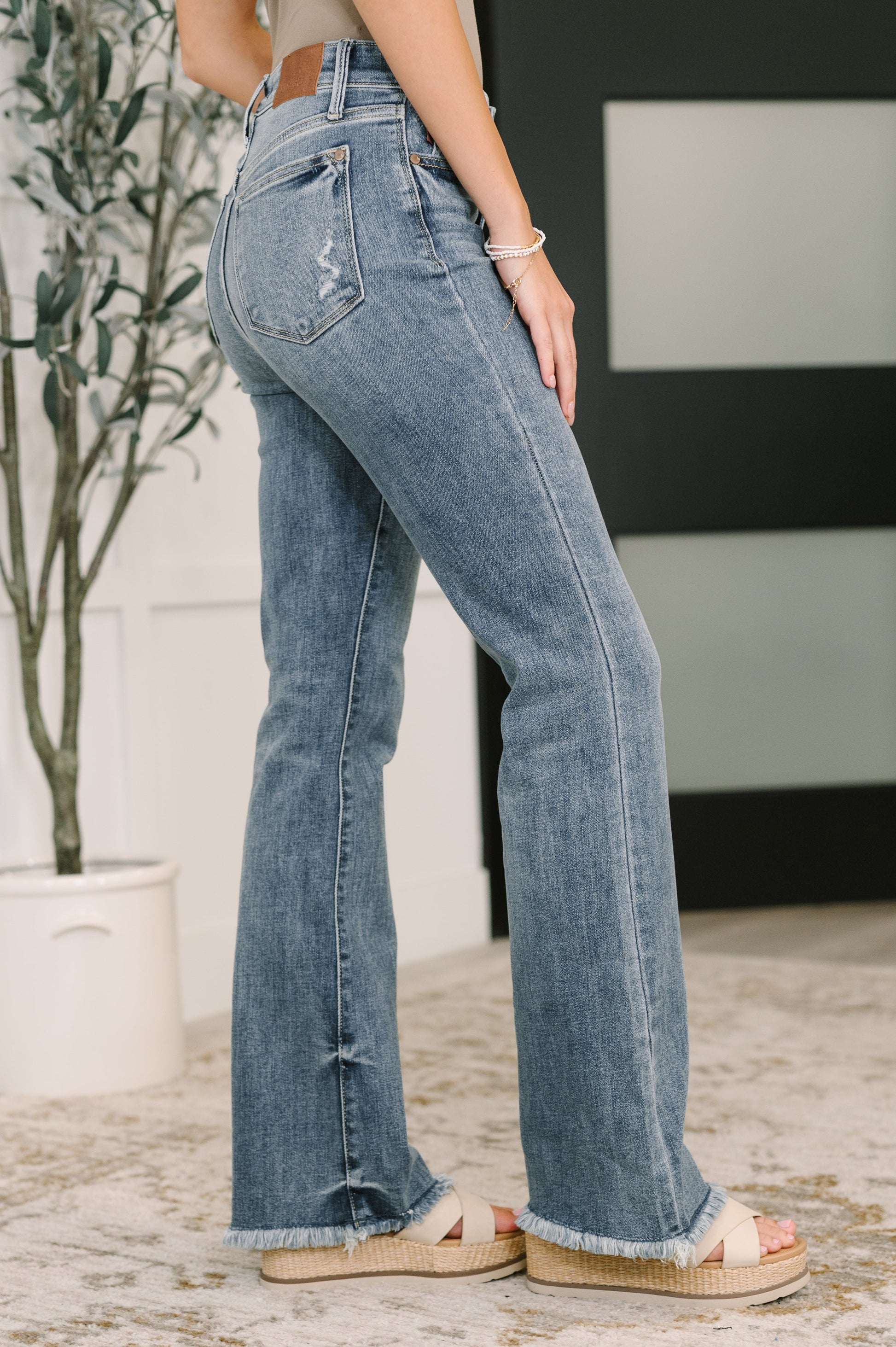 Person wearing blue jeans standing indoors with a plant in the background