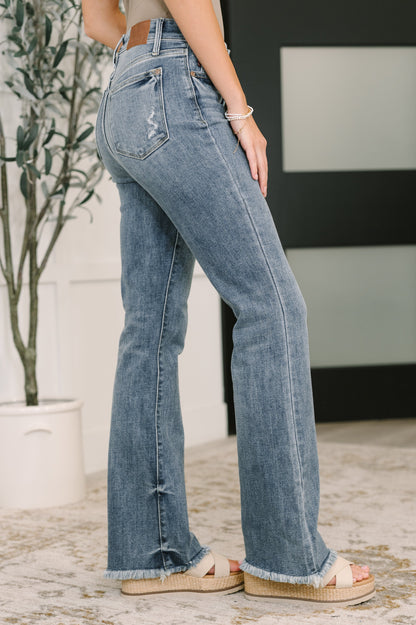Person wearing blue jeans standing indoors with a plant in the background
