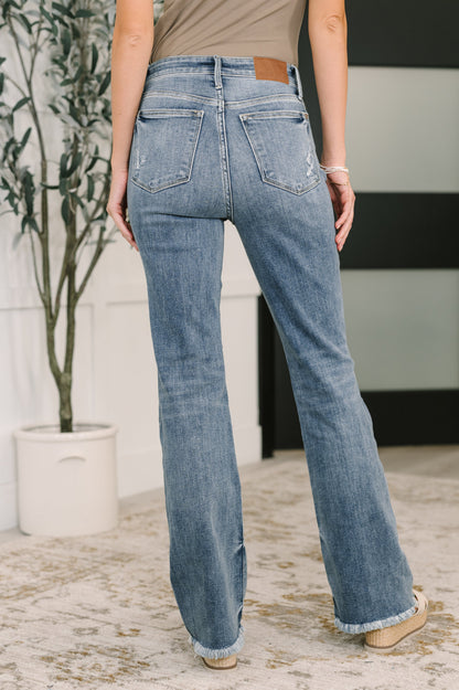 Person wearing blue jeans standing in a room with a plant and wall.