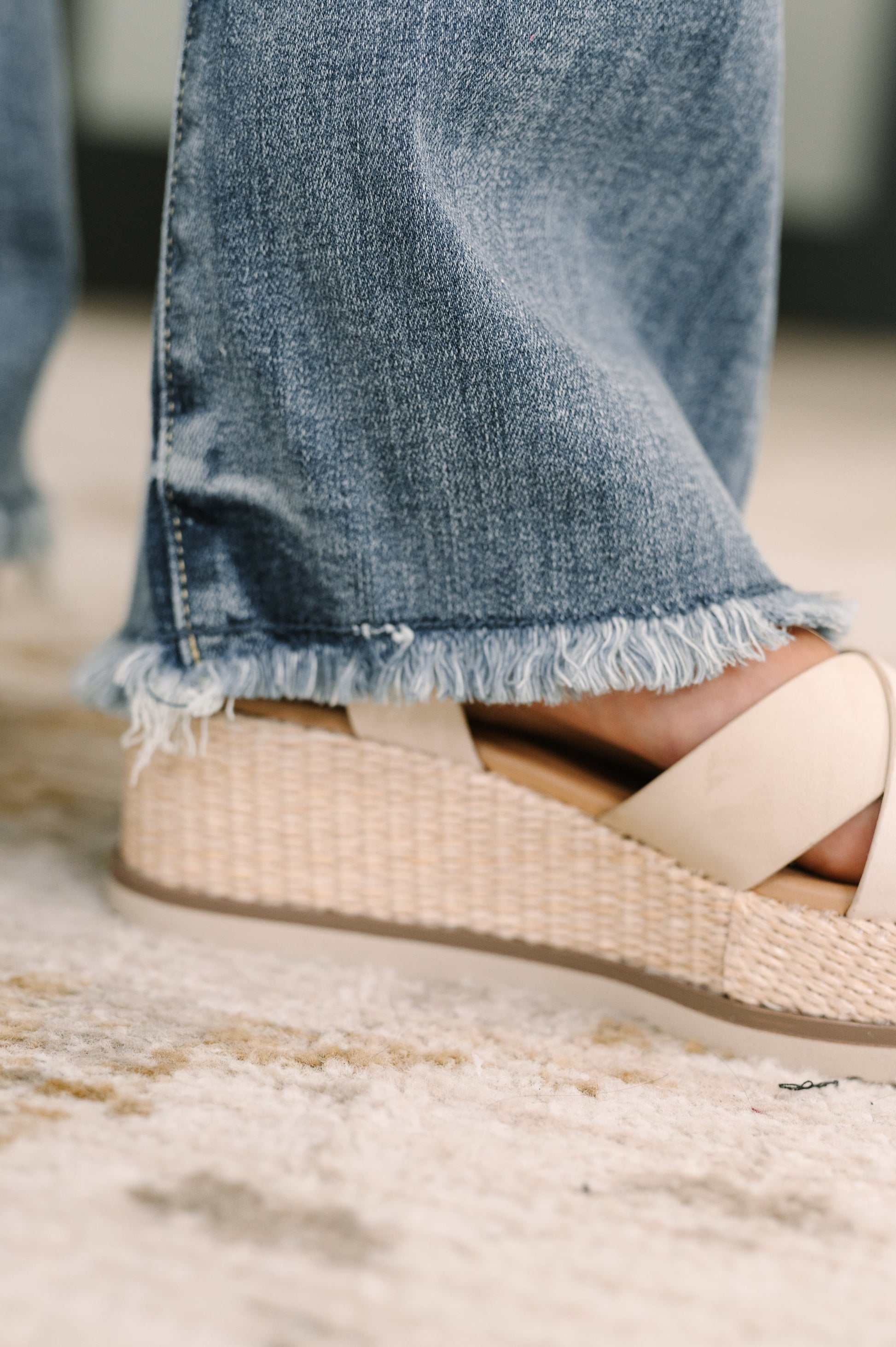 Close-up of a sandal with a woven design worn with blue jeans on a blurred background