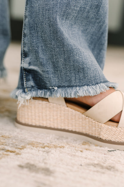 Close-up of a sandal with a woven design worn with blue jeans on a blurred background